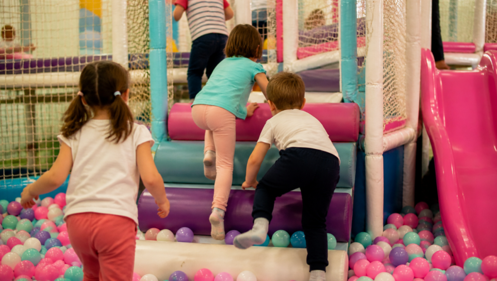 Niños jugando en una zona infantil interior con piscina de bolas y estructuras blandas